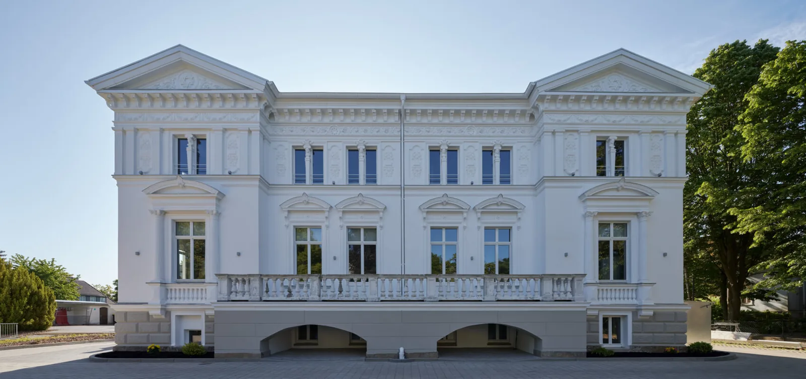 Längsansicht des Rubedo Spa Minden — Stuckvilla mit Sockelarkaden und altem Baumbestand